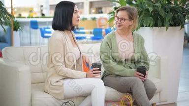 两位美丽的年轻女士在商场购物后休息和讨论一些事情。 喝着外卖咖啡